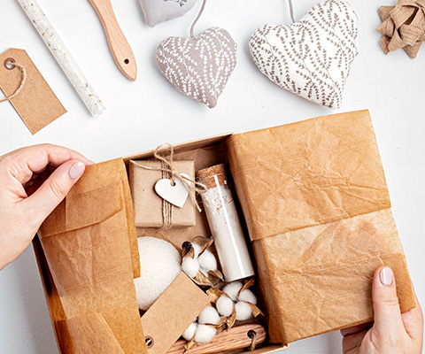 hands opening a gift box filled with brown wrapping paper decorative items natural materials and cotton balls includes rustic elements and sweet designs