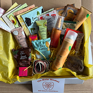 box filled with various skincare and wellness products surrounded by yellow tissue paper featuring Love Nature branding and The Molar Mindset logo showcasing six natural items for self-care and well-being